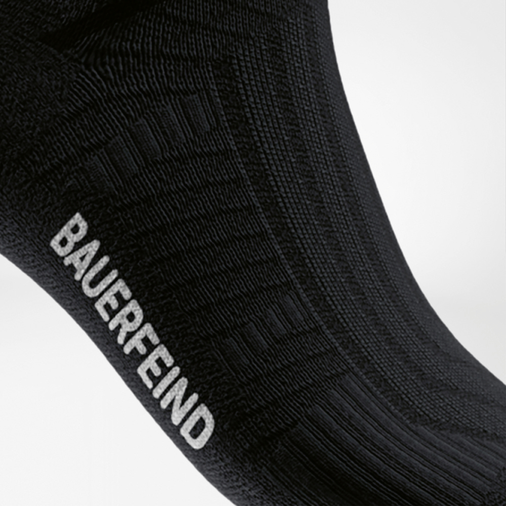 Close-up of the black Run Performance Midcut Sock, side view of the foot with visible “BAUERFEIND” lettering and fine ribbed knit.
