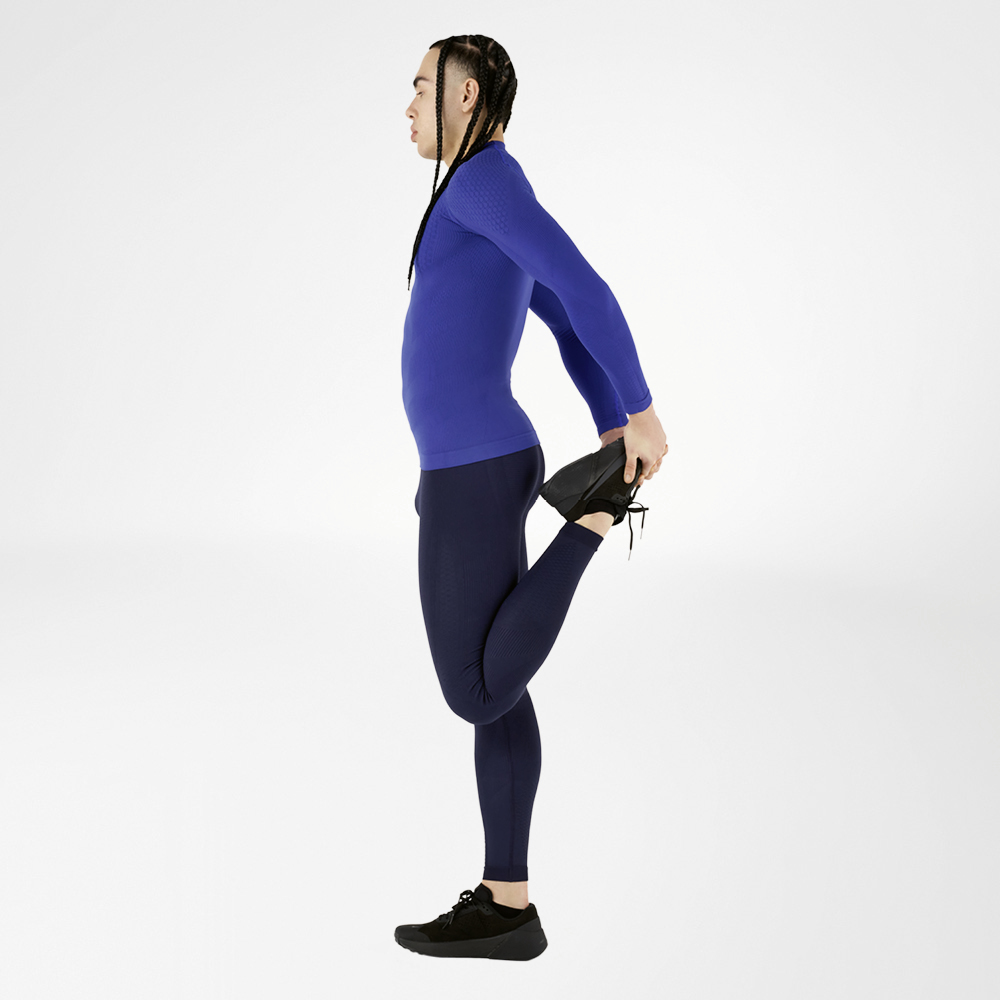Stretch in style - Our complete blue compression sports wear outfit for maximum comfort! An athlete wearing a blue compression sports wear outfit, consisting of a long-sleeve shirt and tights, performs a stretching exercise, holding one leg back, against a white background. The outfit provides high comfort and optimal muscle support.