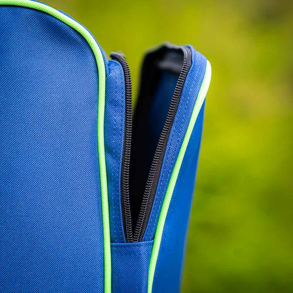 Close-up of the zipper on the Bauerfeind Sports ski boot bag. The black zipper is partially open and framed by a green edge. The blurred background shows greenery, indicating an outdoor setting.