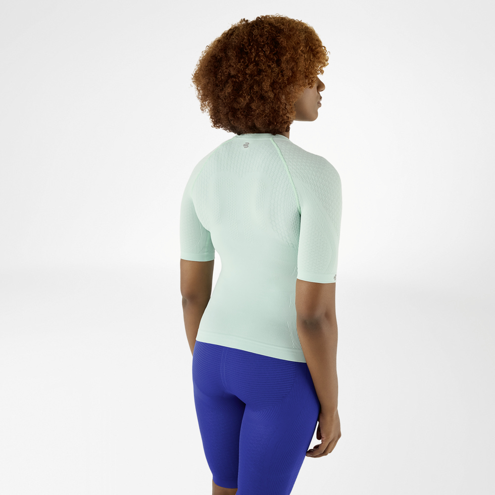 Back view of a woman with curly hair in a mint green compression shirt and blue leggings, looking slightly to the side.