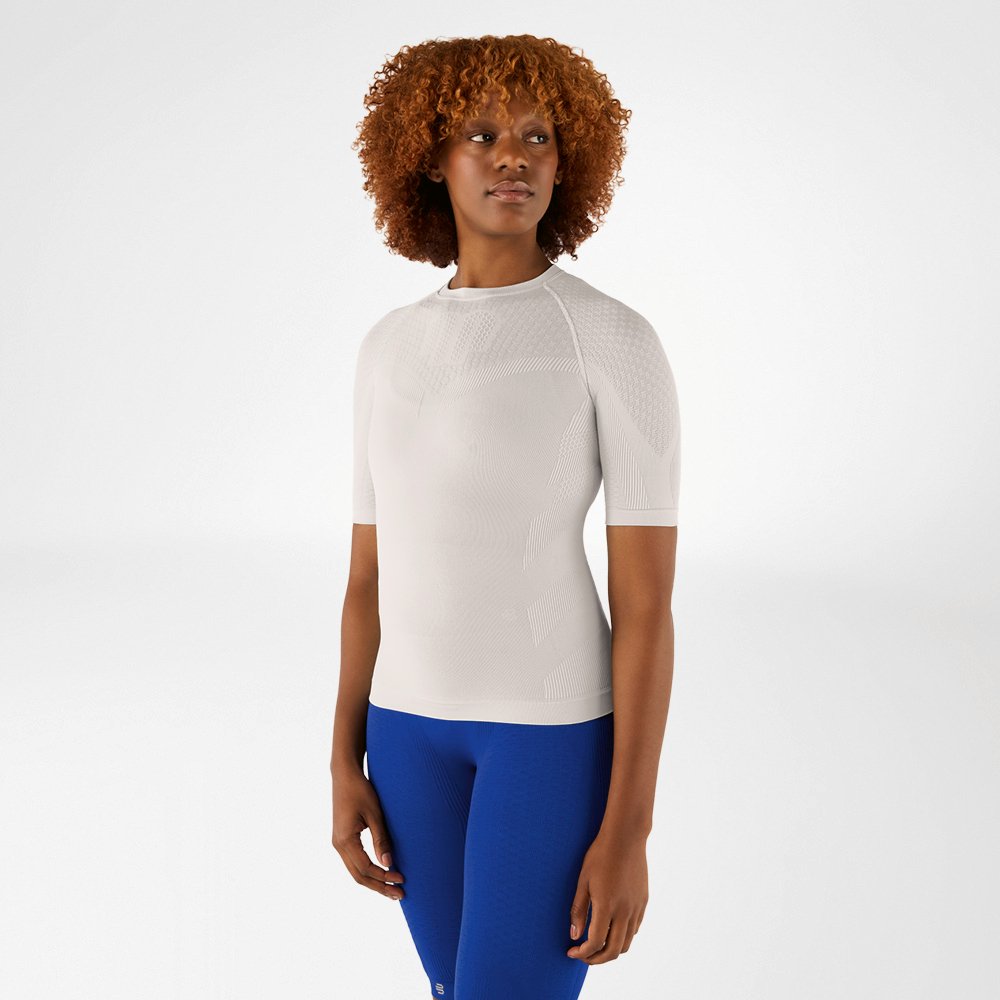 Woman with curly hair in a silver-grey compression shirt and blue leggings. She is standing facing forward and looking to the side.