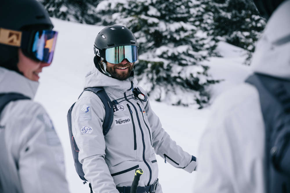 Good, well -being skier with a black helmet gray jacket and backpack recording between two other skiers