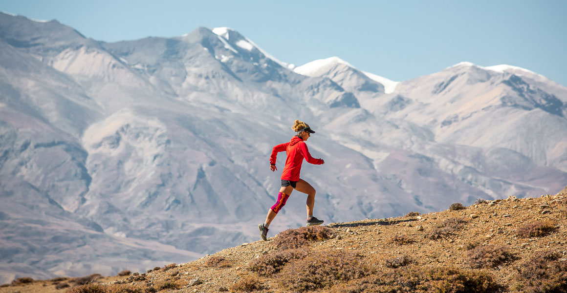 Trailläriner runs up with the Himalayas in the background and wears a knee tandage