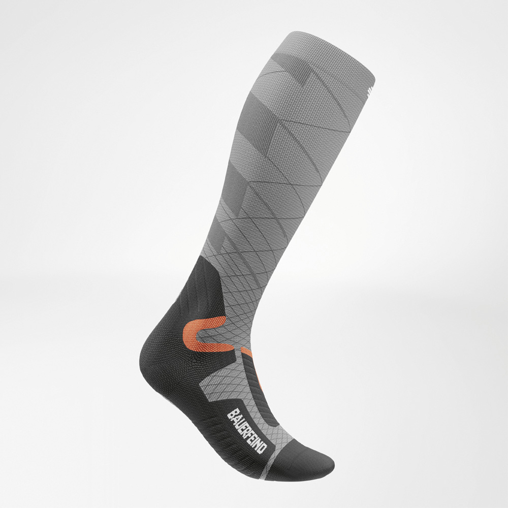 Side view of the women's ski compression sock Women's grey ski compression sock in side view, featuring anatomically optimized fit, sporty look, and contrasting orange and black details.