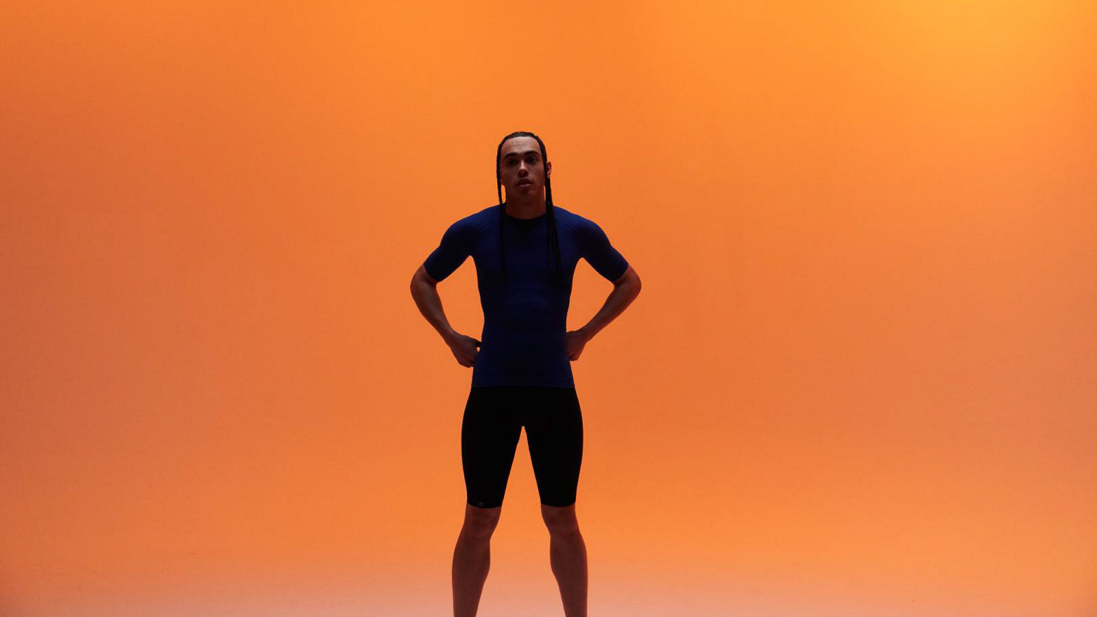 Athlete in blue sportswear with compression shirt and compression pants in front of an orange background.