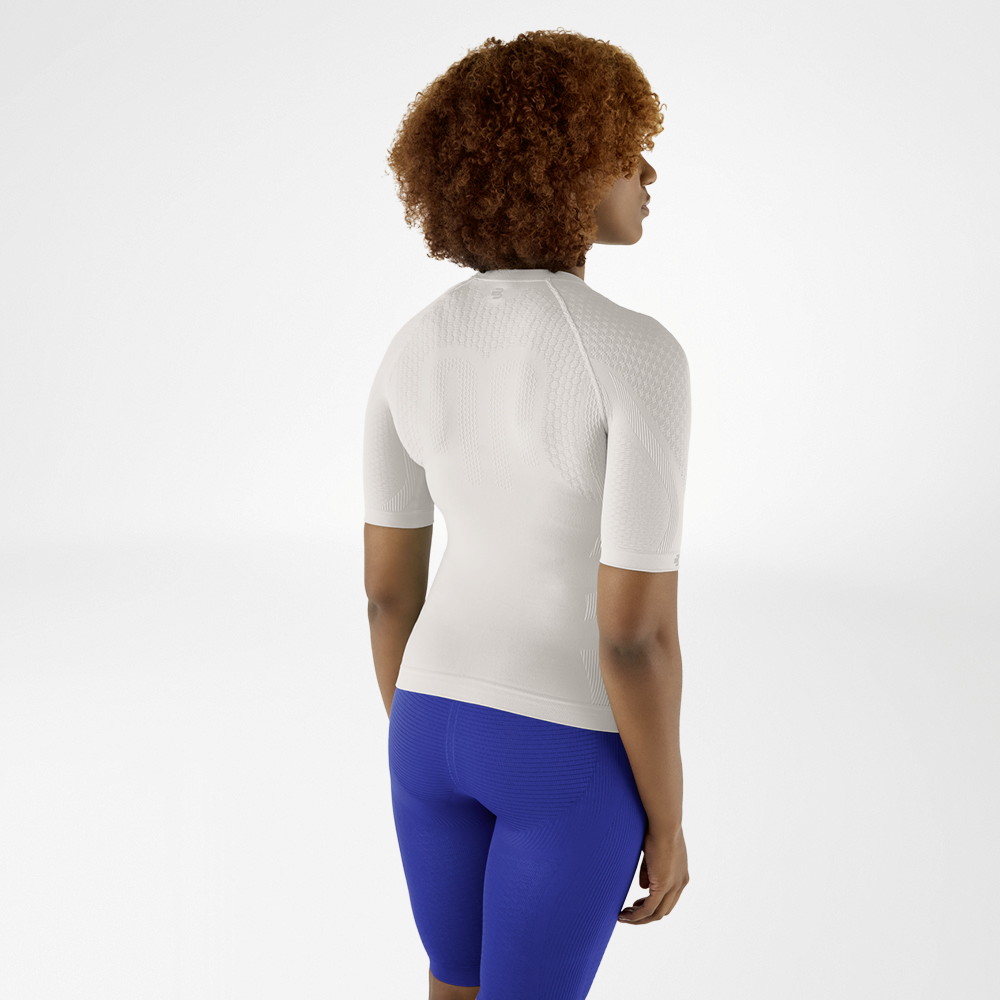 Back view of a woman with curly hair in a silver-grey compression shirt and blue leggings, looking slightly to the side.