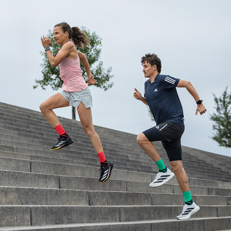 Two women run vigorously through an old town street with small balconies