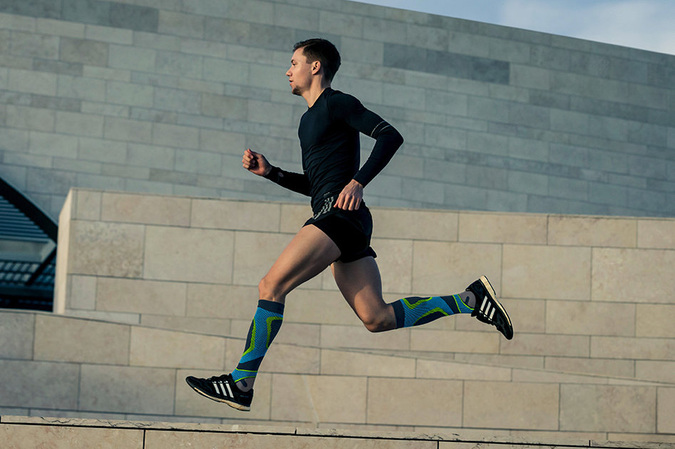 Marathon Trainingsplan Guy Running Through Lisbon Next to Museum Run Performance Compression Socks blue Bauerfeind Sports